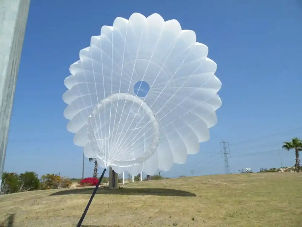 Inflated white round canopy with apex vent, seen from below against a blue sky