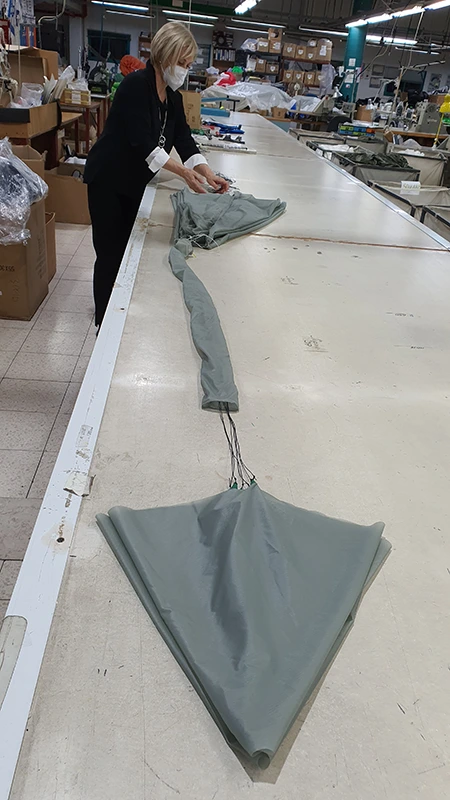 Staff member laying out a grey-green parachute canopy on a long packing table