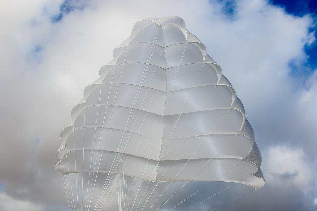 APCO Guided Mayday SLT, a steerable Rogallo-type parachute, open against a cloudy sky