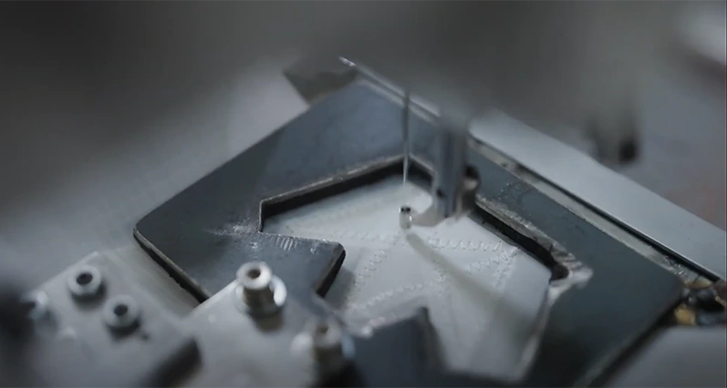 Close-up of an automated sewing machine stitching fabric held in a metal template