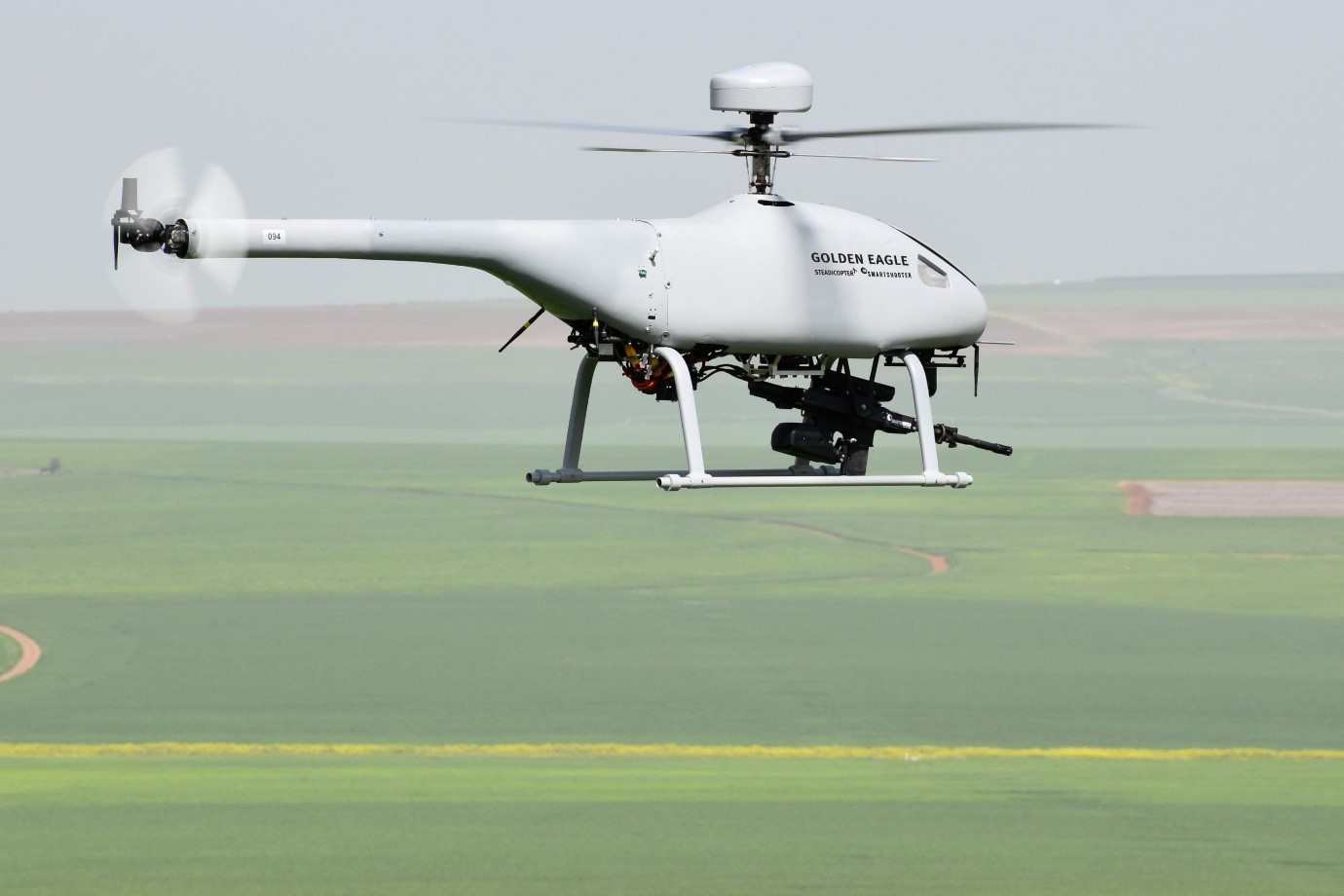 Unmanned helicopter with skid landing gear hovering above a field
