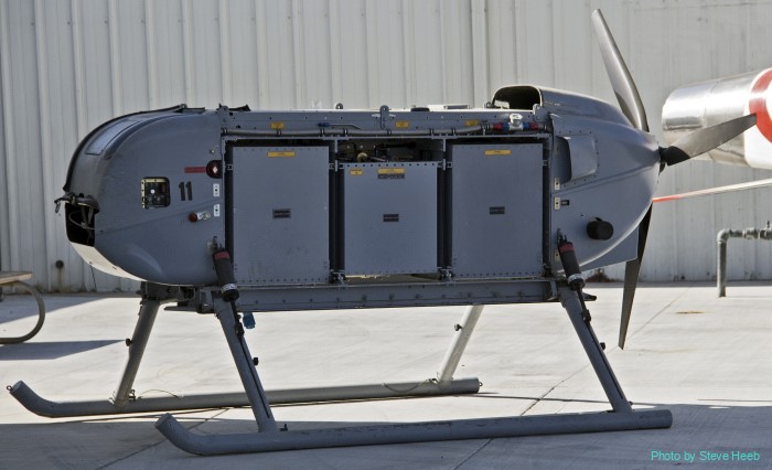 Unmanned paratrike aircraft with side cargo bays and skids in front of a hangar