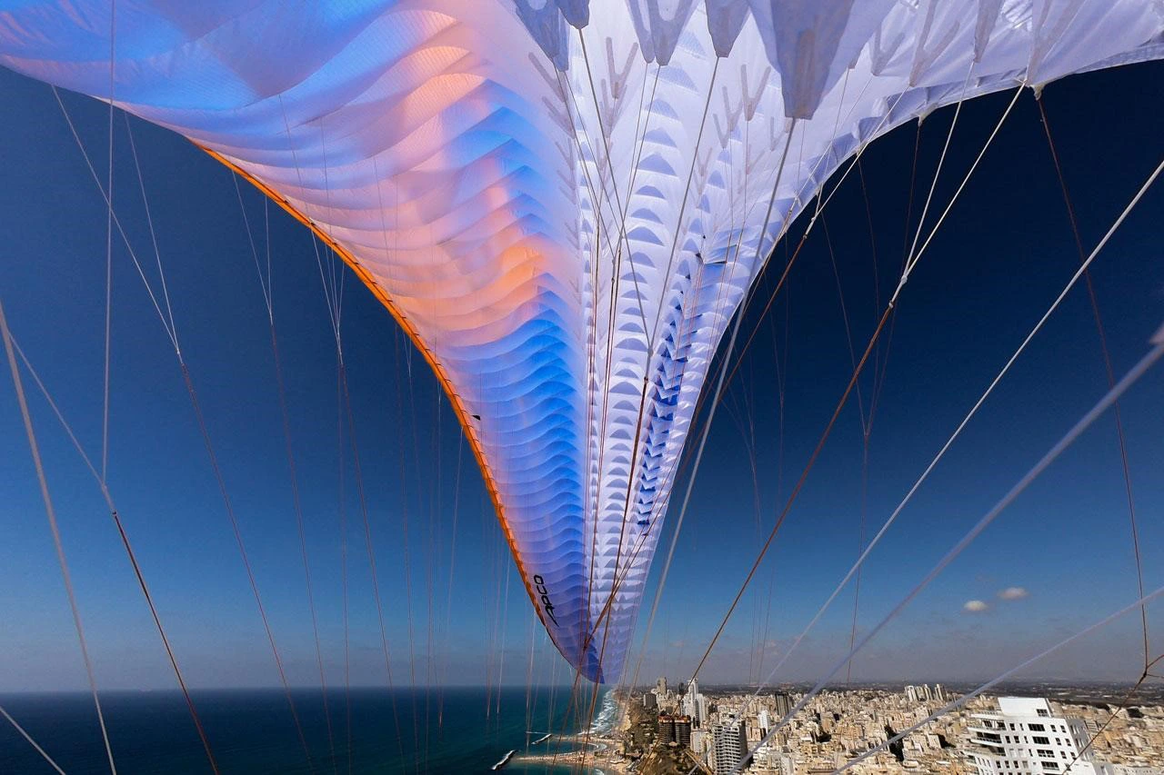 View from below into a paraglider canopy above a coastal city