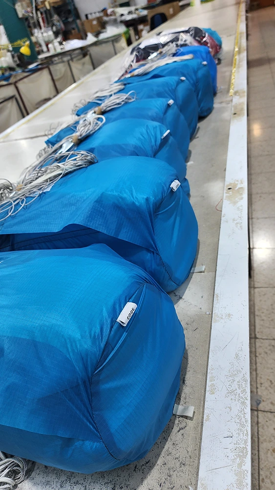 Row of packed blue parachutes with bundled lines on a long packing table in production