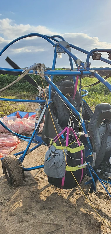 Blue paratrike frame with a parachute container attached to it, a canopy laid out on the field beside it