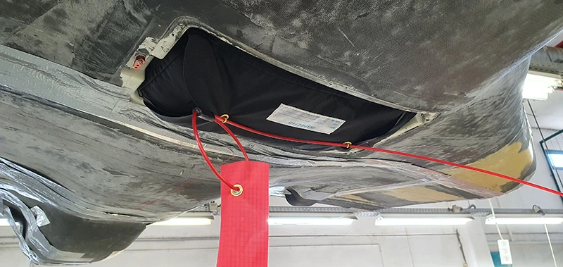 Open parachute bay on the underside of a UAV fuselage with the packed parachute and a red safety tag
