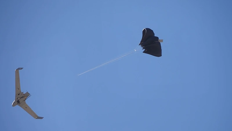 Flying-wing UAV in flight with the recovery parachute being extracted on its bridle behind it
