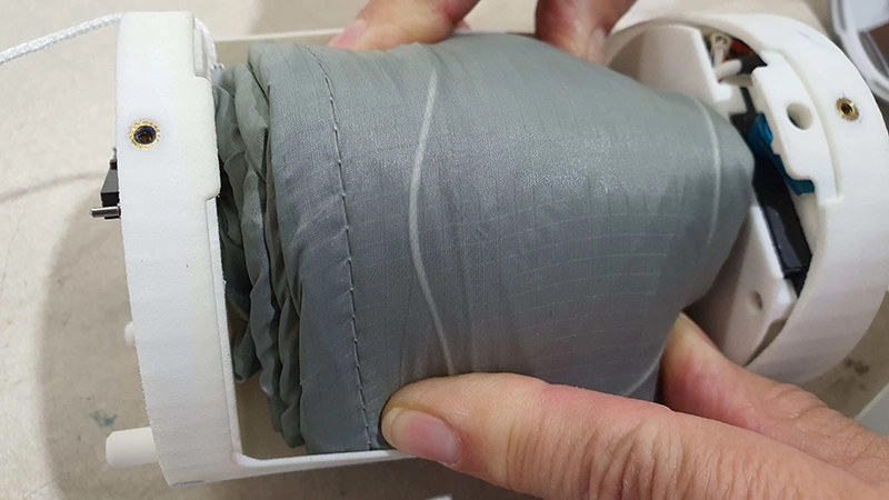 Compactly packed parachute in a grey deployment bag being inserted into a white housing
