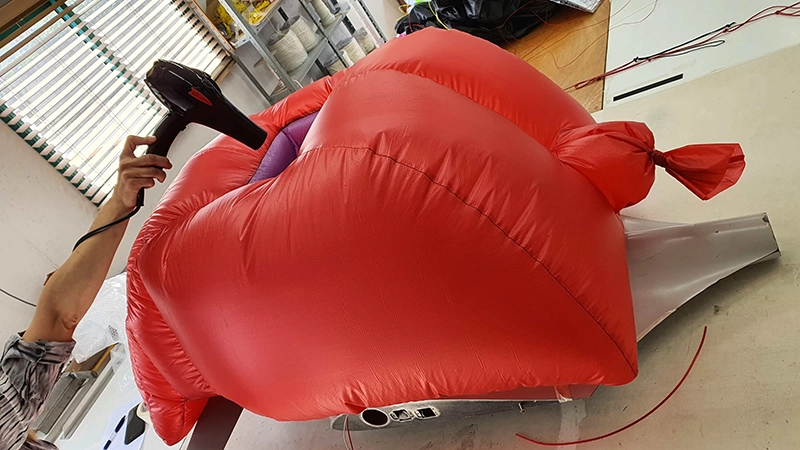 Red ultra-lightweight inflatable part being inflated with a blower on a workbench