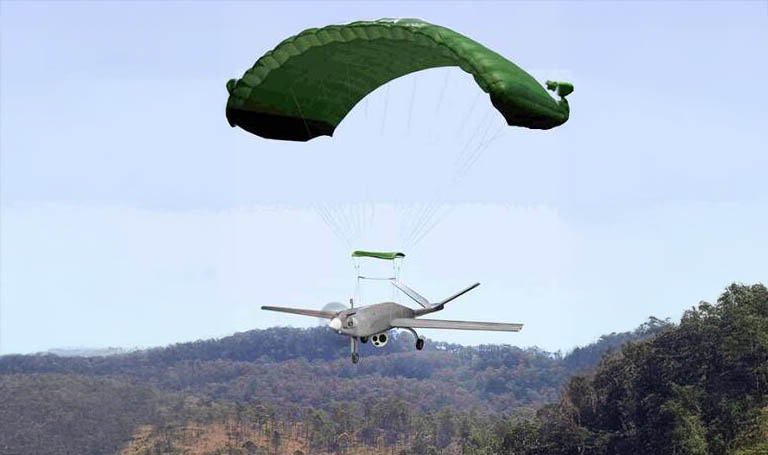 Fixed-wing UAV under a green ram-air parachute above wooded hills