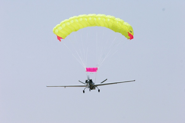 Fixed-wing UAV under a yellow ram air parachute with a pink slider in flight