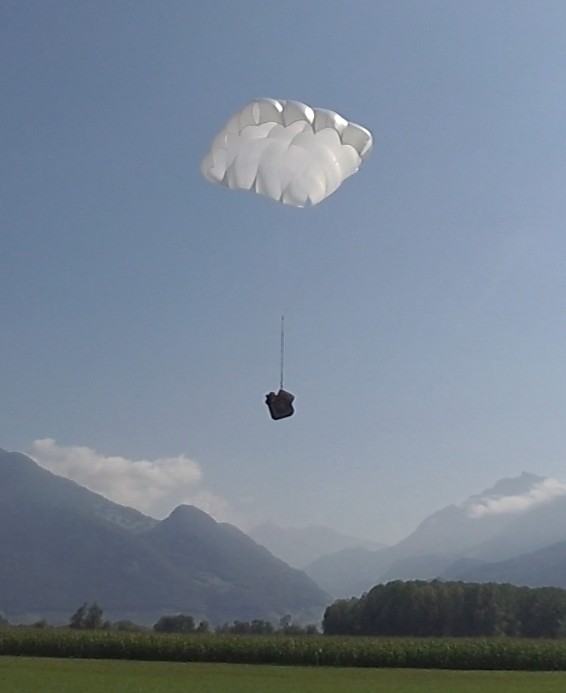White rectangular parachute canopy descending with a suspended load against a mountain backdrop