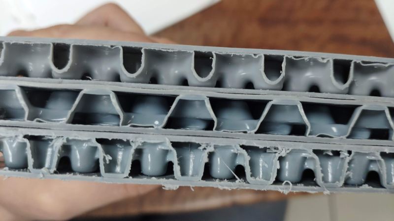 Cross-section of a multi-layer grey plastic crash pad with cellular structure, held in a hand