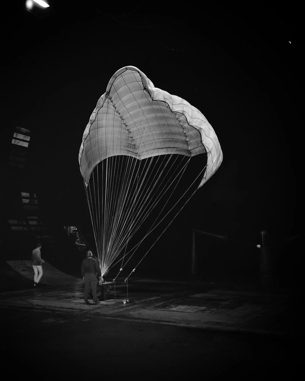 Black-and-white photo of an open Rogallo parachute on the ground with two people beneath it