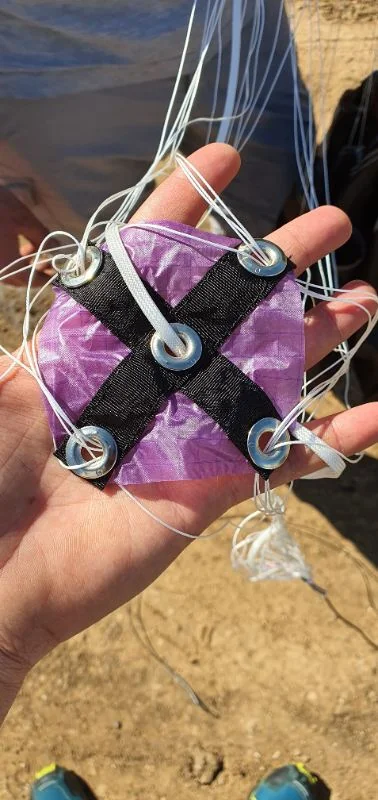 Small purple fabric slider with webbing cross and metal grommets through which the lines run