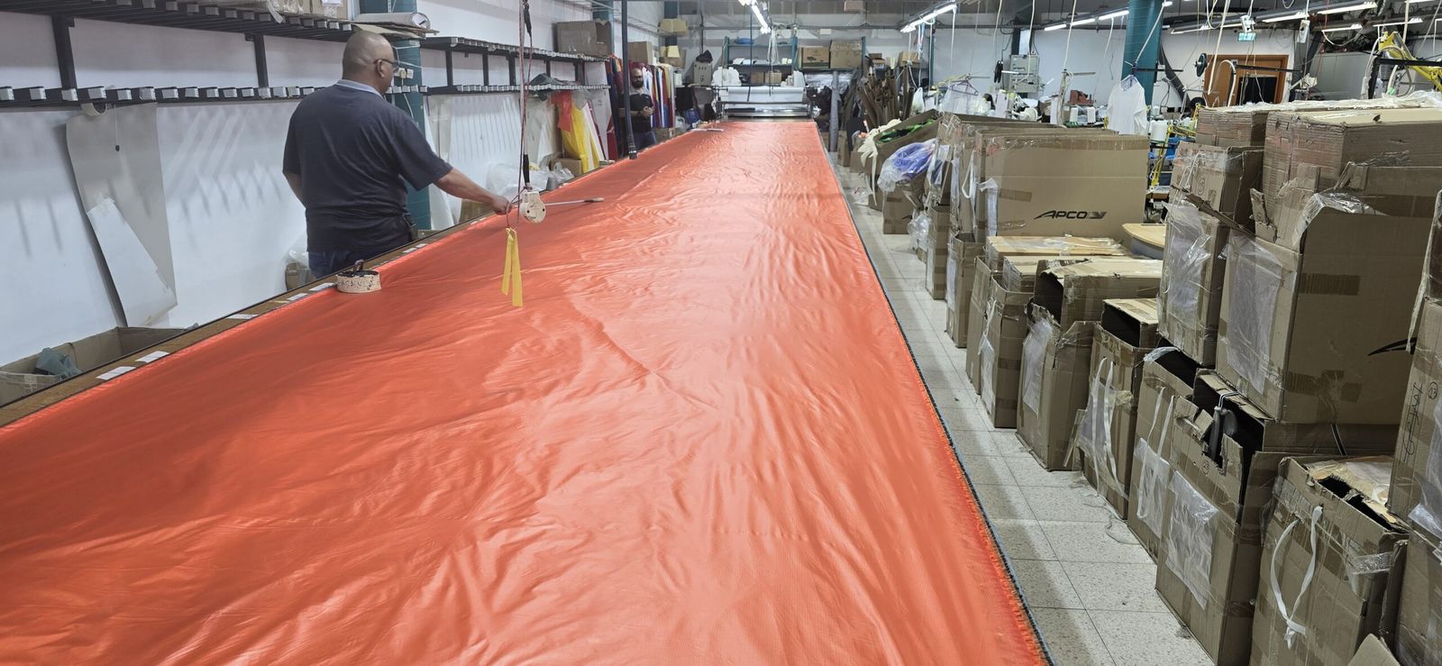 Production hall: an employee lays out a long orange fabric panel on the cutting table, with stacked boxes alongside
